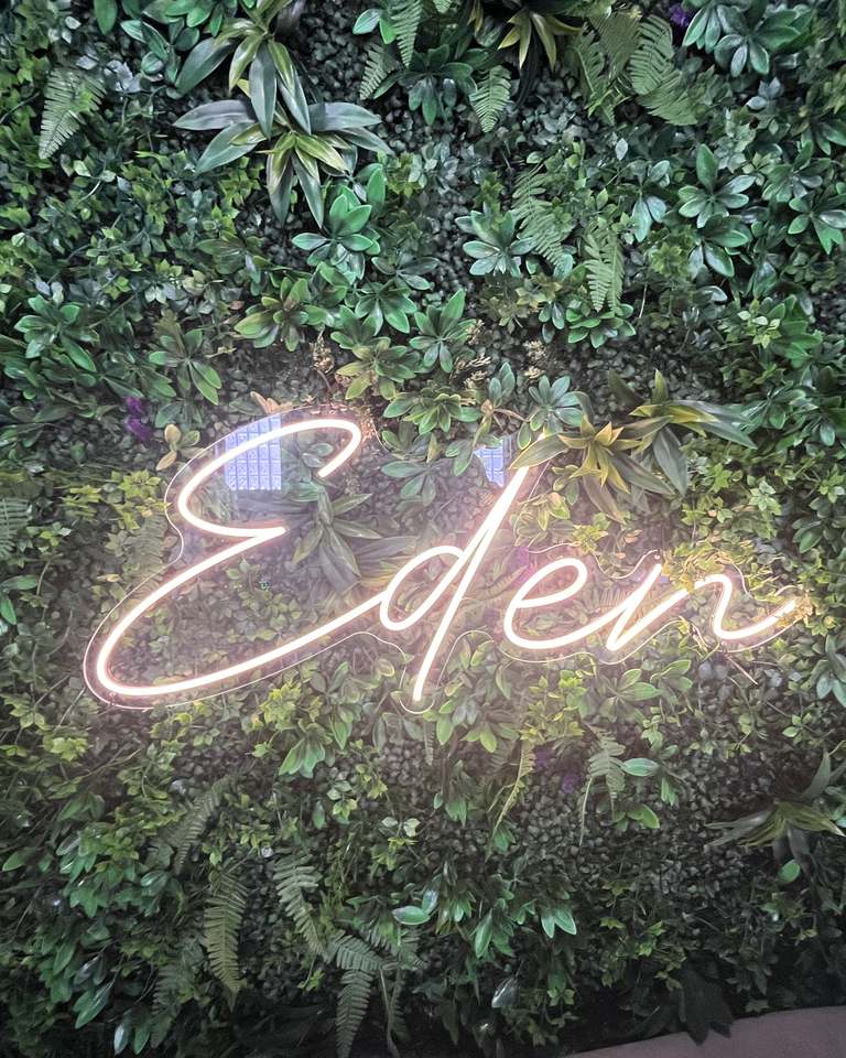 The Eden neon sign glowing on a wall of lush green foliage at Eden 314.