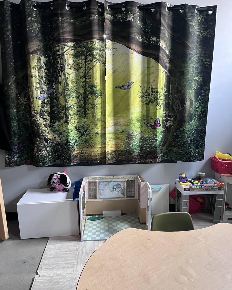 A children's play and reading area with a forest mural, books, and a globe.